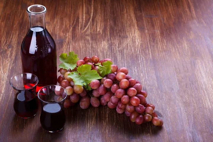 grapes juice with two half filled glass and whole bunch of grapes on a wooden table