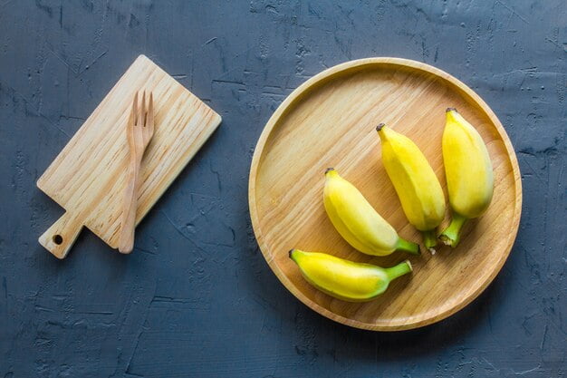 Yelakki banana on a wooden plate on blue table with wooden fork.
