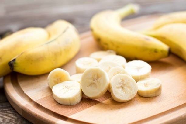 some banana are sliced into small pieces on a wooden cutting board