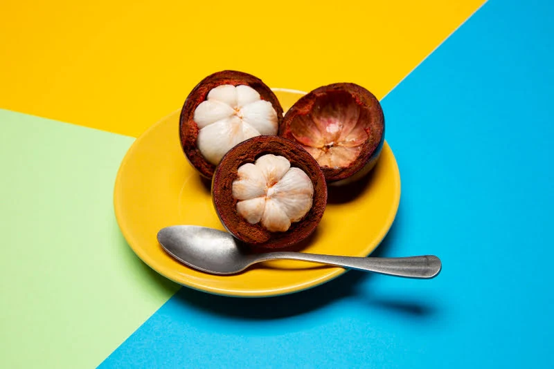 Mangosteen fruit is placed on the plate with a steel spoon on the table.