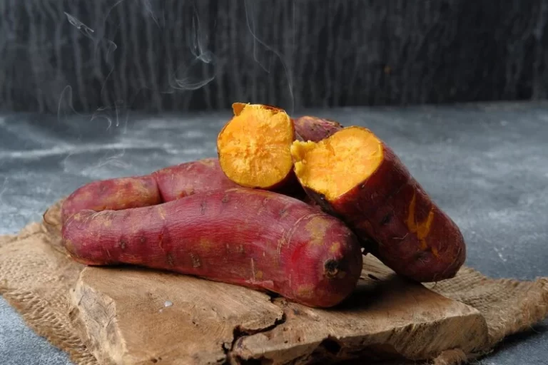 Sweet potatoes on a wooden bark with grey background.
